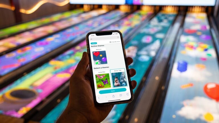 A phone showing the lane theme picker in front of projected bowling lanes, Ventola Projects' projection bowling attraction. Photo: Ventola Projects