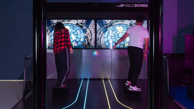 Two riders on ValoBoard tilt boards in front of the game screens, Valo Motion's unmanned mixed-reality attraction. Photo: Valo Motion